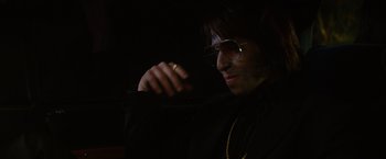 Movie still from “The Nice Guys” (2016), directed by Shane Black – A man in a black shirt and gold jewelry; Close Up shot, Over the shoulder angle