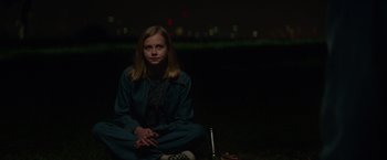 Movie still from “The Nice Guys” (2016), directed by Shane Black – A girl sitting on the ground at night; Medium shot, Low angle