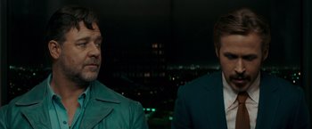 Movie still from “The Nice Guys” (2016), directed by Shane Black – Two men are standing next to each other in front of a city skyline at night; Close Up shot, Over the shoulder angle