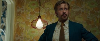 Movie still from “The Nice Guys” (2016), directed by Shane Black – A man standing in front of a floral wallpaper; Close Up shot, Low angle