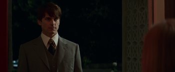 Movie still from “The Nice Guys” (2016), directed by Shane Black – A man wearing a suit and tie standing in front of a building; Close Up shot, Over the shoulder angle