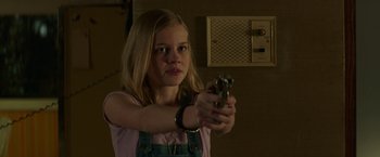 Movie still from “The Nice Guys” (2016), directed by Shane Black – A young girl holding a gun in a room; Close Up shot, Over the shoulder angle