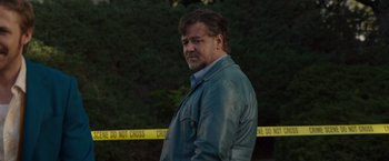 Movie still from “The Nice Guys” (2016), directed by Shane Black – A man standing in front of police tape and trees; Medium shot, Low angle