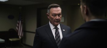 Movie still from “The Night Agent” (2023), created by Shawn Ryan – An older man in a suit and a tie; Close Up shot, Low angle