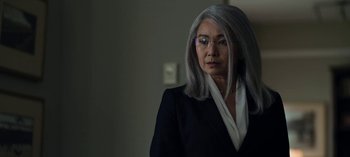 Movie still from “The Night Agent” (2023), created by Shawn Ryan – An older woman with long gray hair wearing a suit; Close Up shot, Over the shoulder angle