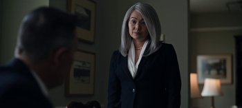Movie still from “The Night Agent” (2023), created by Shawn Ryan – A woman with gray hair wearing a black suit and white shirt; Medium shot, Over the shoulder angle