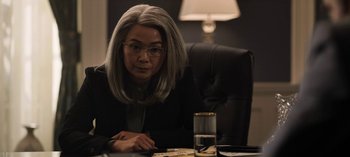 Movie still from “The Night Agent” (2023), created by Shawn Ryan – A woman sitting at a table with a glass of water; Medium shot, Over the shoulder angle