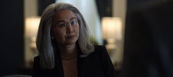 Movie still from “The Night Agent” (2023), created by Shawn Ryan – A woman with gray hair wearing glasses and a black suit; Close Up shot, Over the shoulder angle