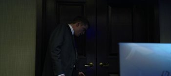 Movie still from “The Night Agent” (2023), created by Shawn Ryan – A man in a suit and tie standing in front of a door; Medium shot, Low angle