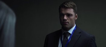 Movie still from “The Night Agent” (2023), created by Shawn Ryan – A man in a suit and tie with a blue lanyard around his neck; Close Up shot, Over the shoulder angle