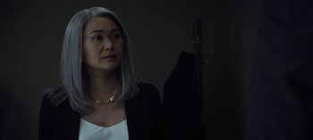 Movie still from “The Night Agent” (2023), created by Shawn Ryan – An older woman wearing a white shirt and a black jacket; Close Up shot, Over the shoulder angle