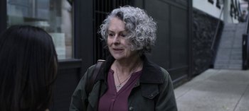 Movie still from “The Night Agent” (2023), created by Shawn Ryan – An older woman with grey curly hair wearing a purple shirt; Close Up shot, High angle
