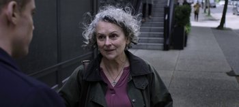 Movie still from “The Night Agent” (2023), created by Shawn Ryan – An older woman with curly white hair standing on the sidewalk; Close Up shot, Over the shoulder angle