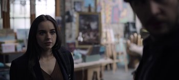 Movie still from “The Night Agent” (2023), created by Shawn Ryan – A woman standing in front of a table with paintings on the wall; Close Up shot, Over the shoulder angle