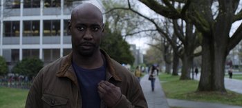 Movie still from “The Night Agent” (2023), created by Shawn Ryan – A man standing on a sidewalk near a tree; Close Up shot, Over the shoulder angle