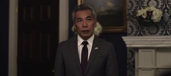 Movie still from “The Night Agent” (2023), created by Shawn Ryan – A man wearing a suit and tie standing in front of a painting; Close Up shot, Low angle