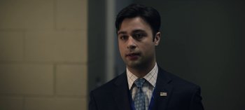 Movie still from “The Night Agent” (2023), created by Shawn Ryan – A man in a suit and tie standing next to a wall; Close Up shot, Over the shoulder angle