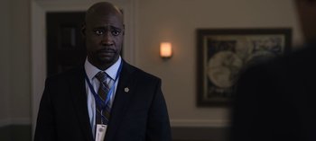 Movie still from “The Night Agent” (2023), created by Shawn Ryan – A man in a suit and tie standing in front of a wall; Close Up shot, Over the shoulder angle