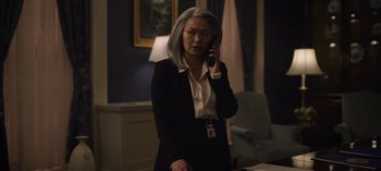 Movie still from “The Night Agent” (2023), created by Shawn Ryan – An older woman talking on a phone in a dark room; Medium shot, Over the shoulder angle