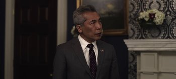 Movie still from “The Night Agent” (2023), created by Shawn Ryan – A man in a suit and tie standing in front of a painting; Close Up shot, Over the shoulder angle