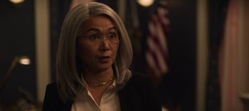 Movie still from “The Night Agent” (2023), created by Shawn Ryan – An older woman wearing a white shirt and a black jacket; Close Up shot, Over the shoulder angle