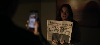 Movie still from “The Night Agent” (2023), created by Shawn Ryan – A woman holding up a newspaper in front of a cell phone; Close Up shot, Over the shoulder angle