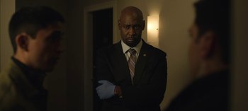 Movie still from “The Night Agent” (2023), created by Shawn Ryan – A man in a suit and tie standing in front of a wall; Medium shot, Low angle