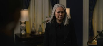Movie still from “The Night Agent” (2023), created by Shawn Ryan – A woman with long gray hair wearing a black jacket; Medium shot, Over the shoulder angle