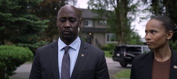 Movie still from “The Night Agent” (2023), created by Shawn Ryan – A man in a suit and tie standing in front of a house; Close Up shot, Over the shoulder angle