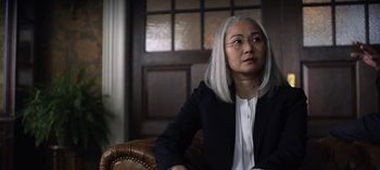 Movie still from “The Night Agent” (2023), created by Shawn Ryan – An older asian woman sitting in a chair; Close Up shot, Over the shoulder angle