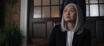 Movie still from “The Night Agent” (2023), created by Shawn Ryan – An older woman sitting on a couch looking up at the sky; Close Up shot, Low angle