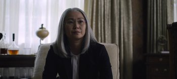 Movie still from “The Night Agent” (2023), created by Shawn Ryan – An older woman with long gray hair sitting in a chair; Close Up shot, Over the shoulder angle