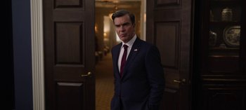 Movie still from “The Night Agent” (2023), created by Shawn Ryan – A man in a suit and tie standing in a room; Medium shot, Over the shoulder angle