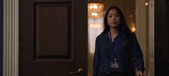 Movie still from “The Night Agent” (2023), created by Shawn Ryan – A woman standing in front of a door wearing a name tag; Medium shot, Over the shoulder angle