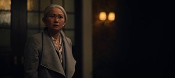 Movie still from “The Night Agent” (2023), created by Shawn Ryan – An older woman standing in front of a building; Close Up shot, Over the shoulder angle