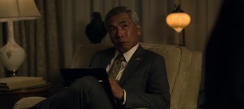 Movie still from “The Night Agent” (2023), created by Shawn Ryan – An older man in a suit and tie sitting in a chair; Close Up shot, Over the shoulder angle