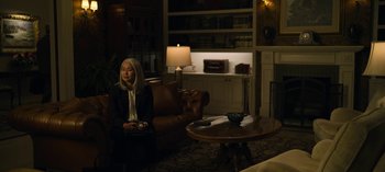 Movie still from “The Night Agent” (2023), created by Shawn Ryan – A woman sitting on a couch in a living room; Wide shot, High angle