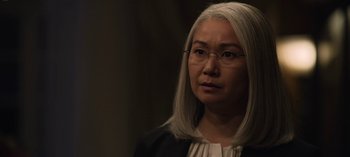 Movie still from “The Night Agent” (2023), created by Shawn Ryan – An older woman wearing glasses and a black jacket; Close Up shot, Over the shoulder angle