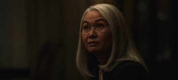 Movie still from “The Night Agent” (2023), created by Shawn Ryan – An older woman wearing glasses looking to her left; Close Up shot, Over the shoulder angle