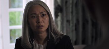 Movie still from “The Night Agent” (2023), created by Shawn Ryan – An older woman wearing glasses and a jacket; Close Up shot, Over the shoulder angle