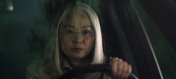 Movie still from “The Night Agent” (2023), created by Shawn Ryan – An older woman with glasses is holding a steering wheel; Close Up shot, Low angle