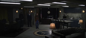 Movie still from “The Night Agent” (2023), created by Shawn Ryan – Two people standing in a room with a lamp on the floor; Wide shot, High angle