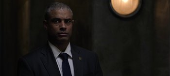 Movie still from “The Night Agent” (2023), created by Shawn Ryan – A man in a suit and tie standing next to a wall; Close Up shot, Over the shoulder angle