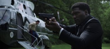 Movie still from “The Night Agent” (2023), created by Shawn Ryan – A man in a suit and tie holding a gun in his hand; Medium shot, Over the shoulder angle