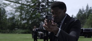 Movie still from “The Night Agent” (2023), created by Shawn Ryan – A man in a suit and tie holding a camera; Close Up shot, Over the shoulder angle