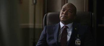 Movie still from “The Night Agent” (2023), created by Shawn Ryan – A man in a suit and tie sitting in a chair; Close Up shot, Low angle