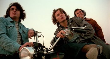 Movie still from “The Other Side of the Wind” (2018), directed by Orson Welles – A group of people sitting on a motorcycle; Medium shot, Low angle
