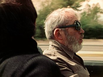 Movie still from “The Other Side of the Wind” (2018), directed by Orson Welles – An older man wearing sunglasses driving a car; Close Up shot, Over the shoulder angle