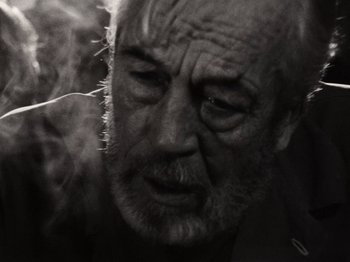 Movie still from “The Other Side of the Wind” (2018), directed by Orson Welles – An old man with a beard is smoking a cigarette; Close Up shot, Low angle