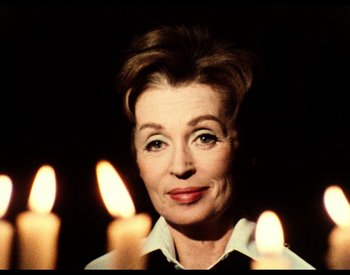 Movie still from “The Other Side of the Wind” (2018), directed by Orson Welles – An older woman is standing in front of some candles; Close Up shot, Low angle